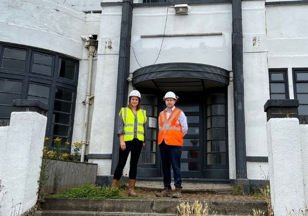 Two people in hi-viz gear standing at the doorway to a hotel renovation.