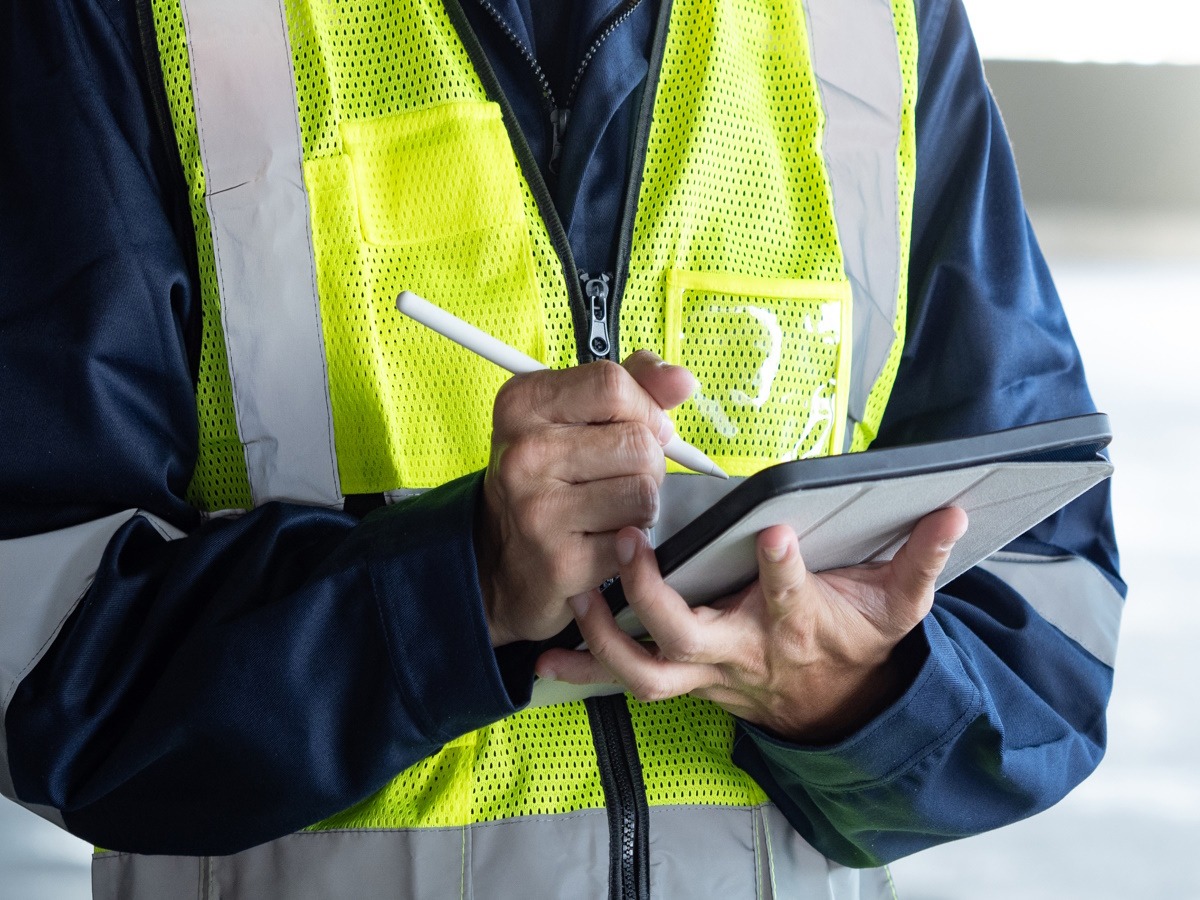 SHEQ advisor in hi-vis clothing writing on tablet.